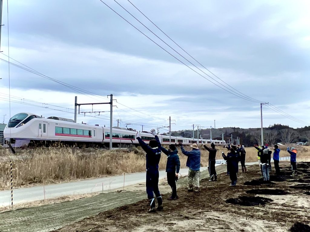 富岡駅前の「駅東圃場」。ボランティアの方々と通過する電車に手を振り、富岡町の印象を残す。乗客も手を振り返してつかの間の交流を楽しむ。